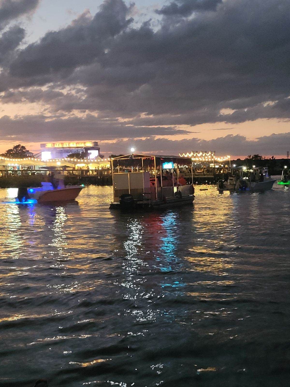 Dusk harbor with small boats on rippling water and city lights glowing beneath dark clouds