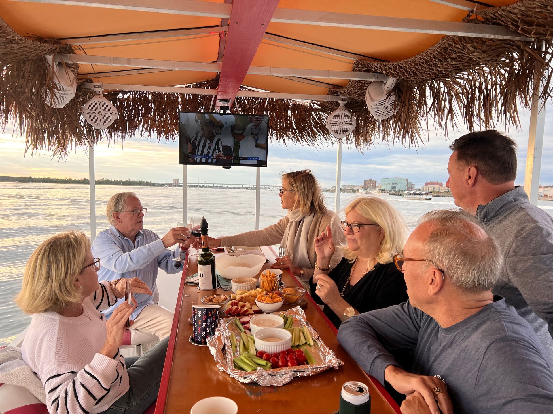 Friends dining together on a boat deck at sunset, with food, drinks, and ocean views