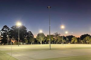 A basketball court is lit up at night with trees in the background.