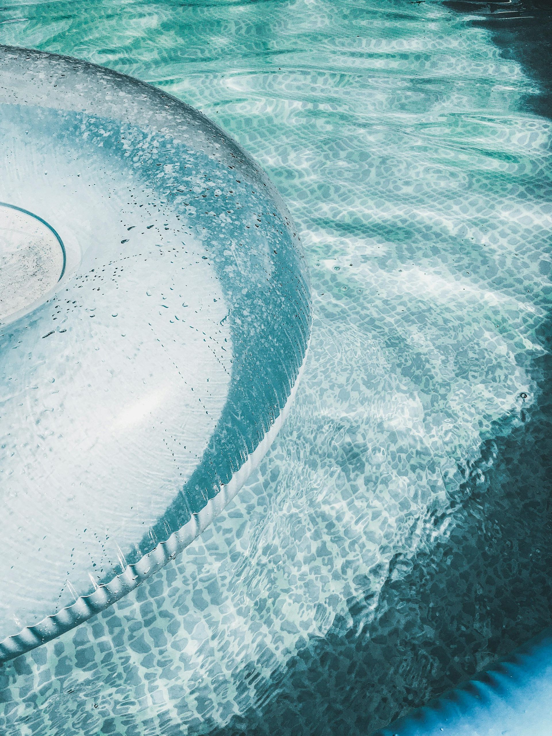 A high-angle view of a circular step in a swimming pool with shimmering turquoise water and a tiled edge.