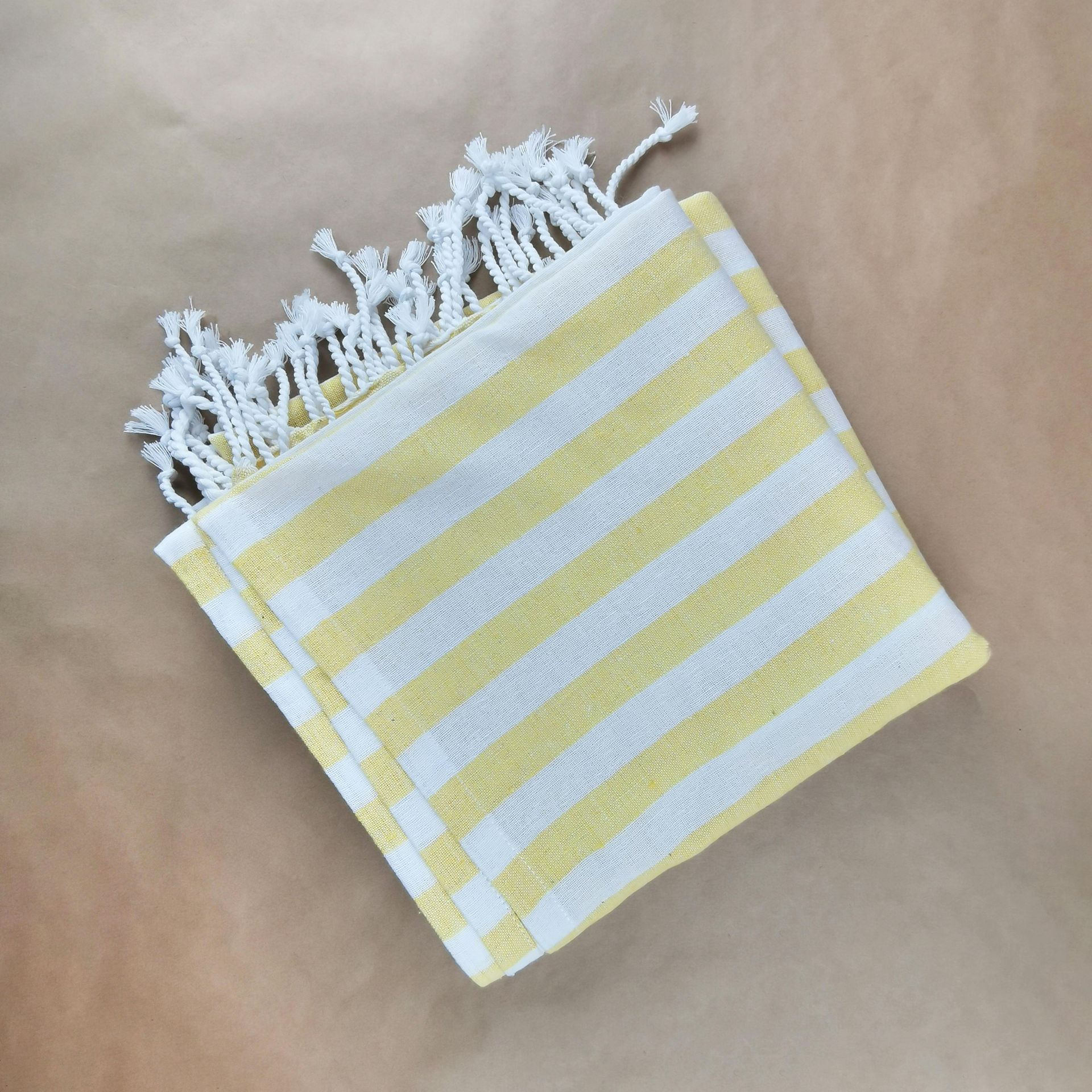 A folded white towel with yellow stripes and tasseled edges, centered on a light brown background.