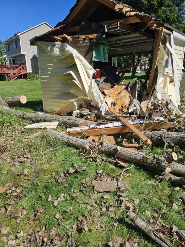 Collapsed shed with debris and fallen tree limbs in a grassy yard near a house