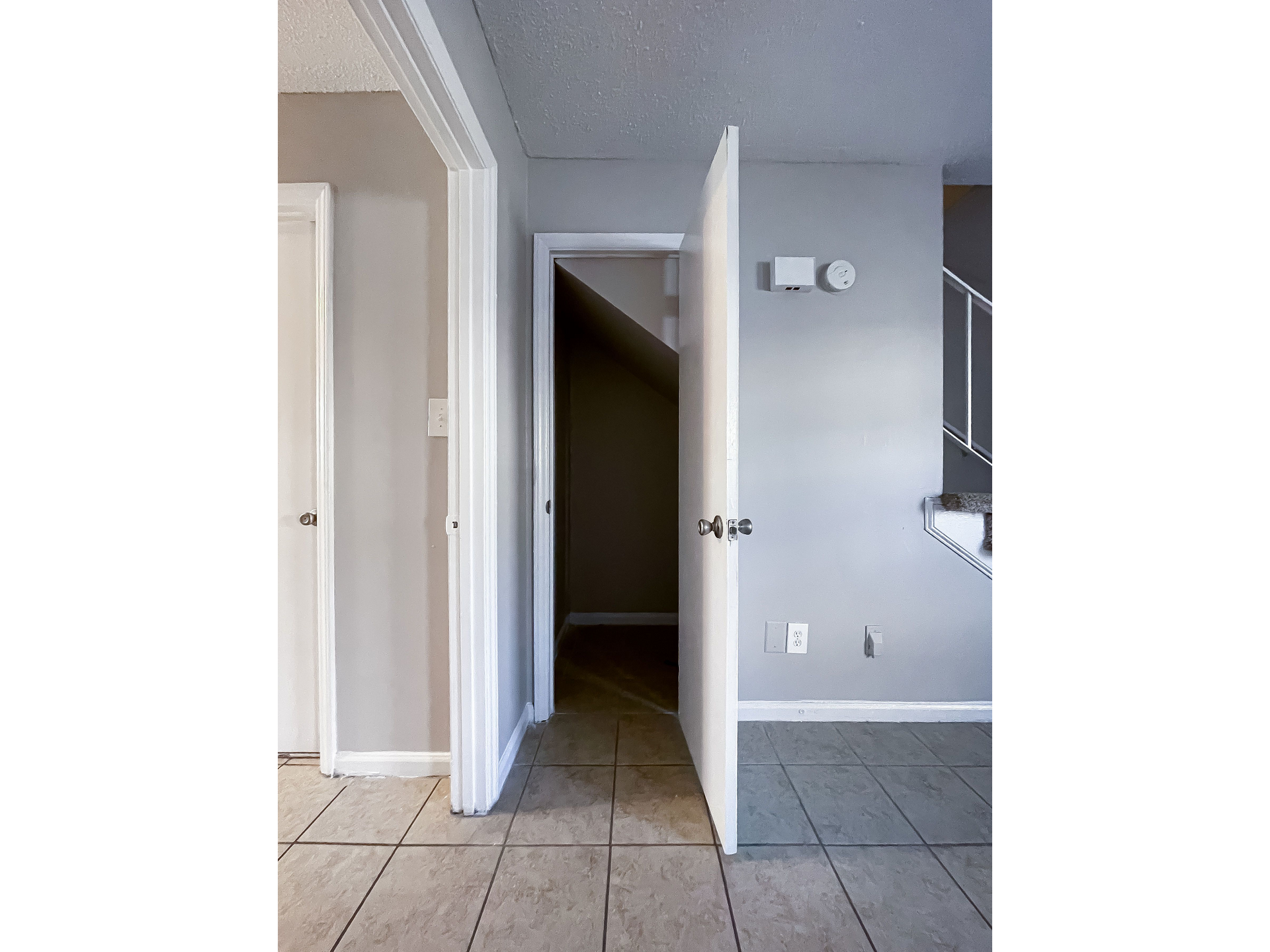 Empty apartment interior: tiled entry with an open door and stairs on the right.
