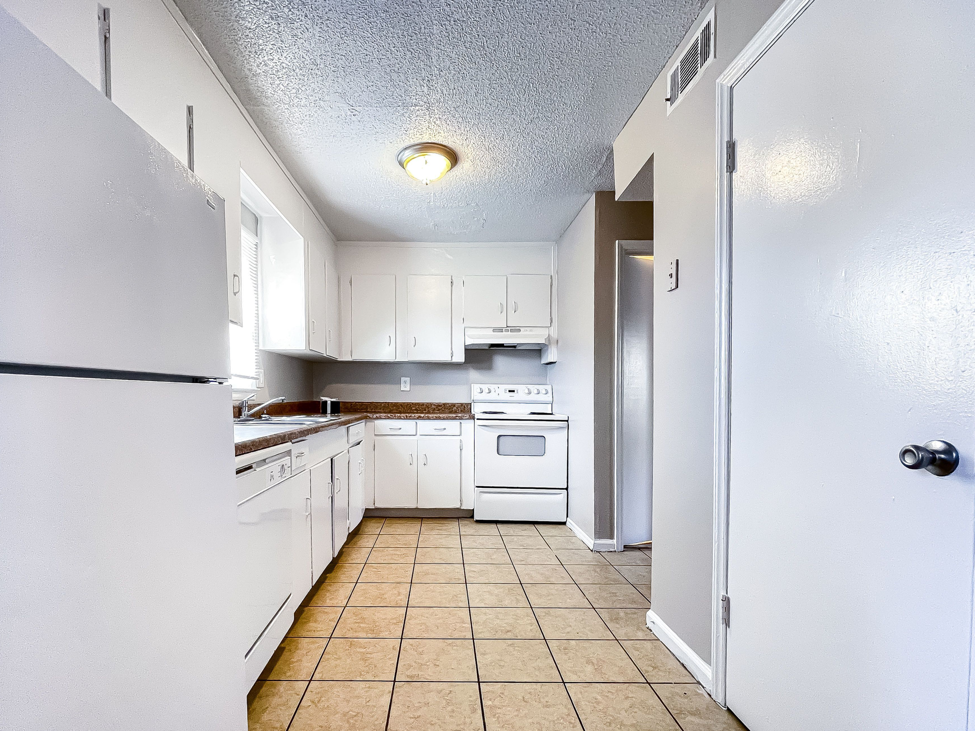 Interior view of a white kitchen in an apartment, with white cabinets, a stove, and tiled floor.