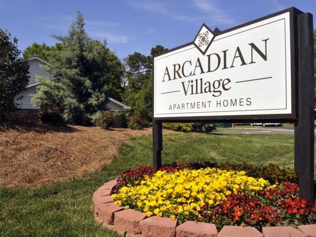 Monument sign for Arcadian Village Apartment Homes with a colorful flower bed.