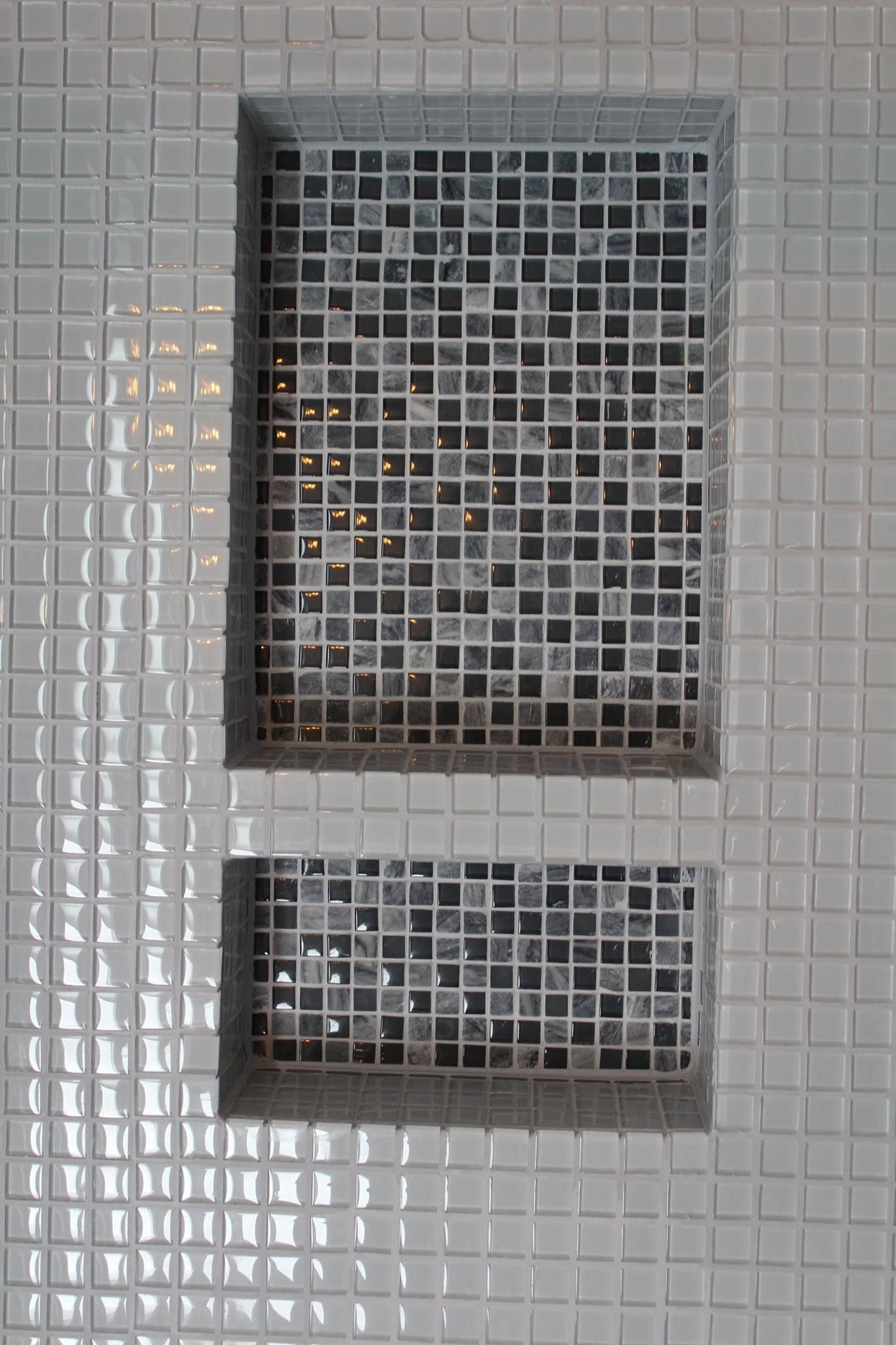 Gray tiled wall with two recessed square mosaic tile shelves.