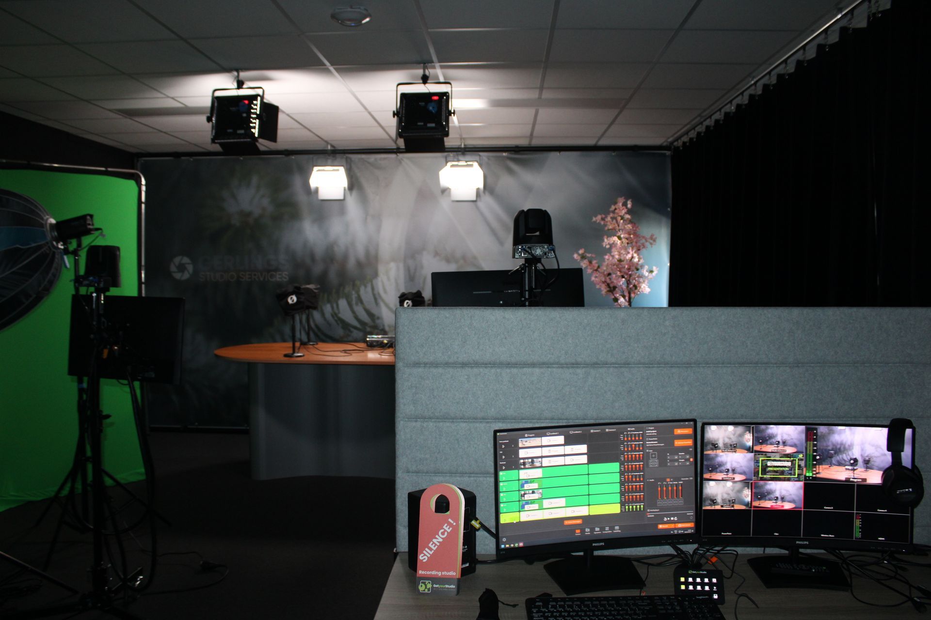 Televisiestudio met groen scherm, bedieningspaneel, camera's en achtergronddecor.