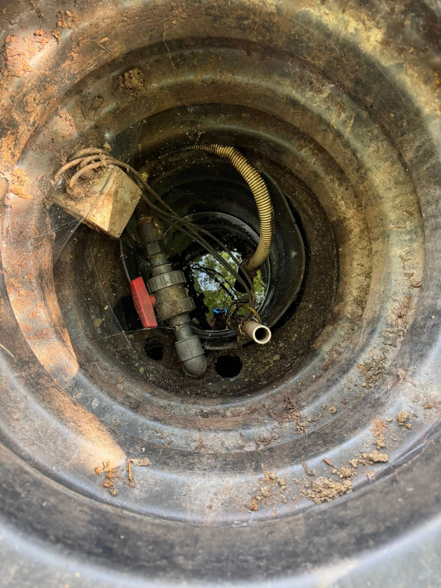Inside a round pipe or drain, showing a hose and debris in a dark opening.