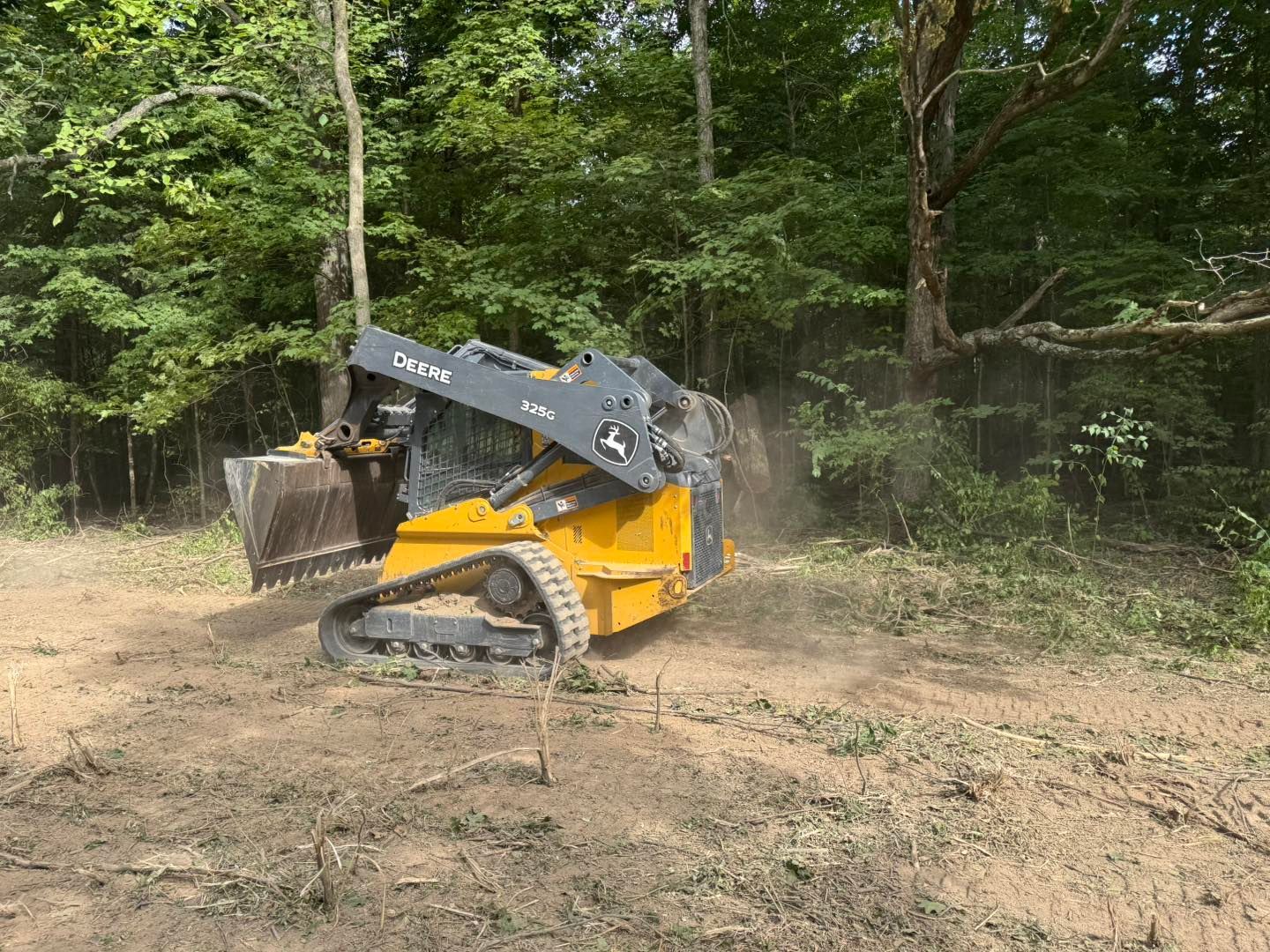 Yellow compact track loader with raised bucket in a wooded clearing