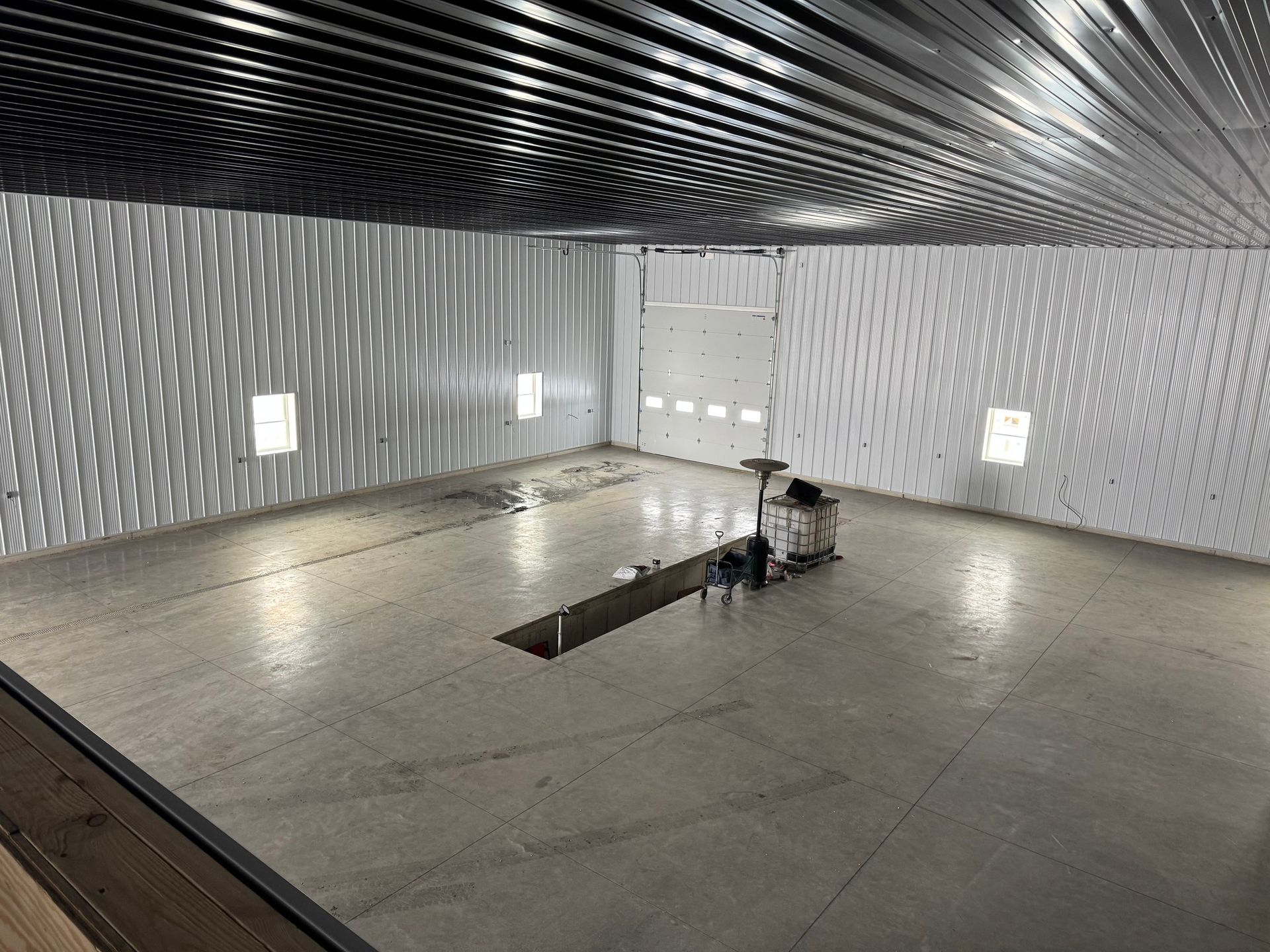 Empty industrial room with concrete floor, white walls, and a reflective metal ceiling panel.