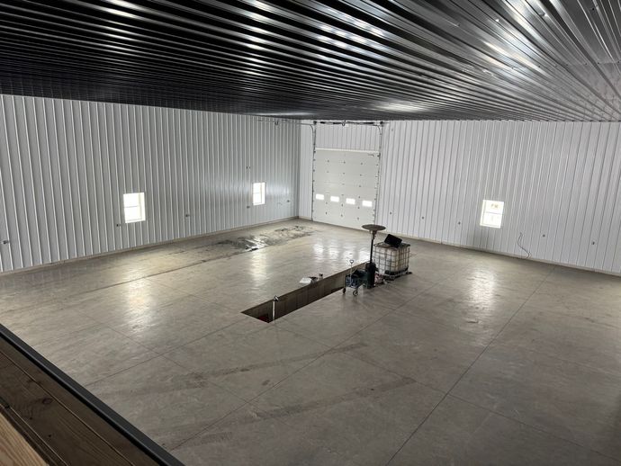 Empty metallic test chamber with concrete floor, bright wall lights, and a small machine near a floor opening