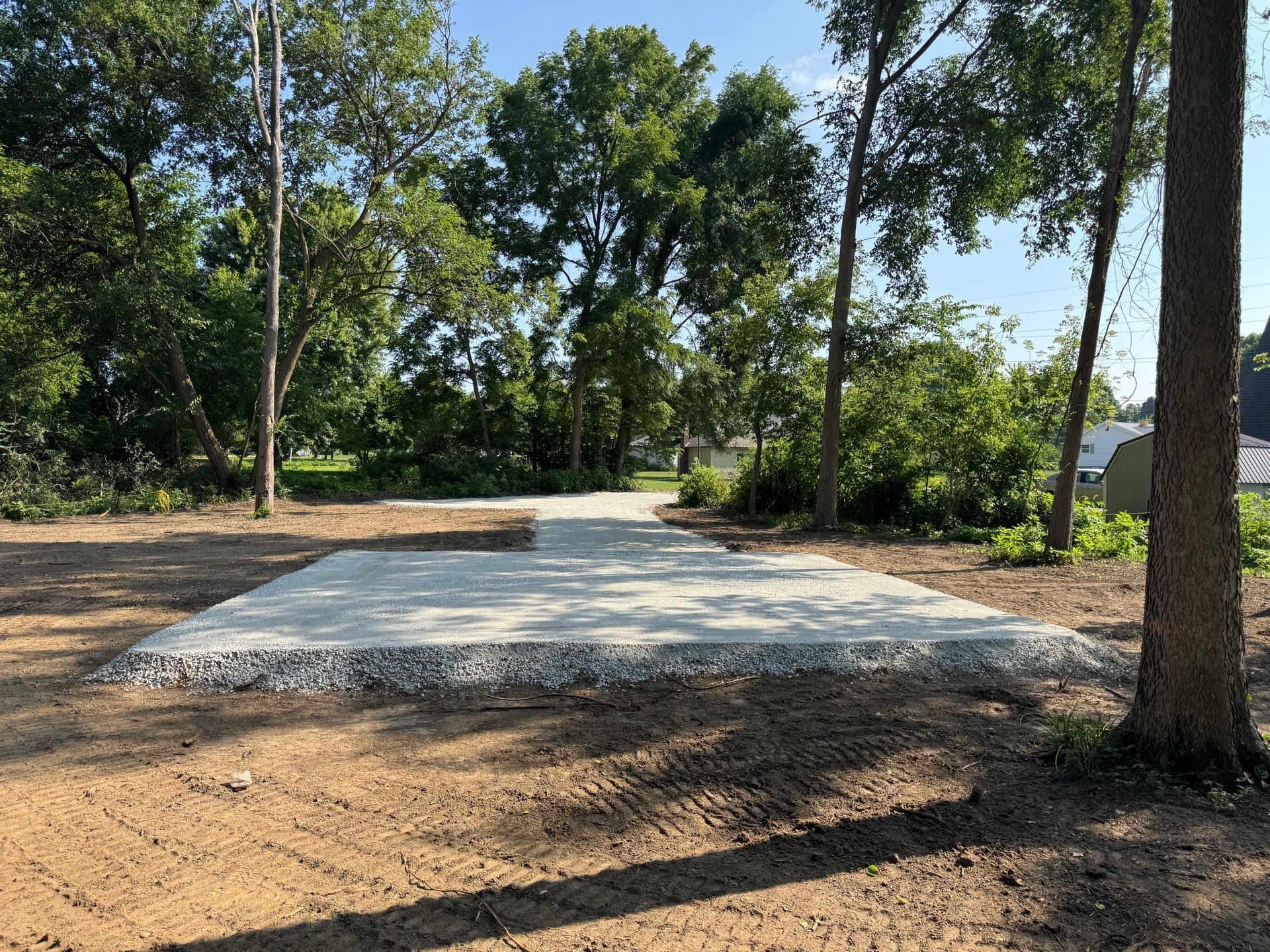 Gravel pad in a wooded park area with trees and a dirt clearing around it