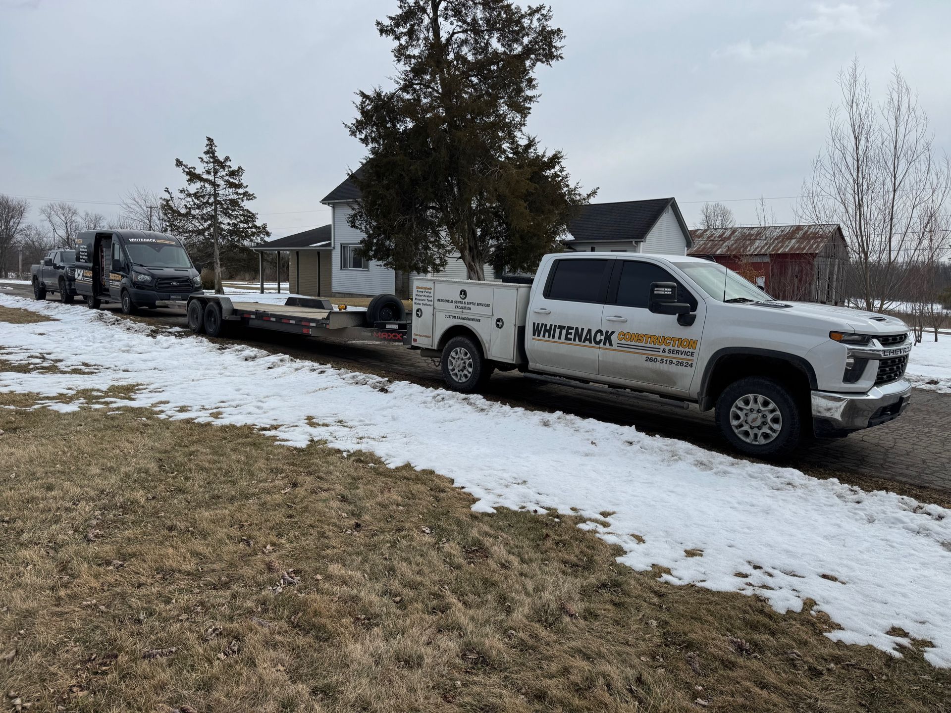 White utility truck towing a trailer on a snowy roadside with other vehicles parked behind it