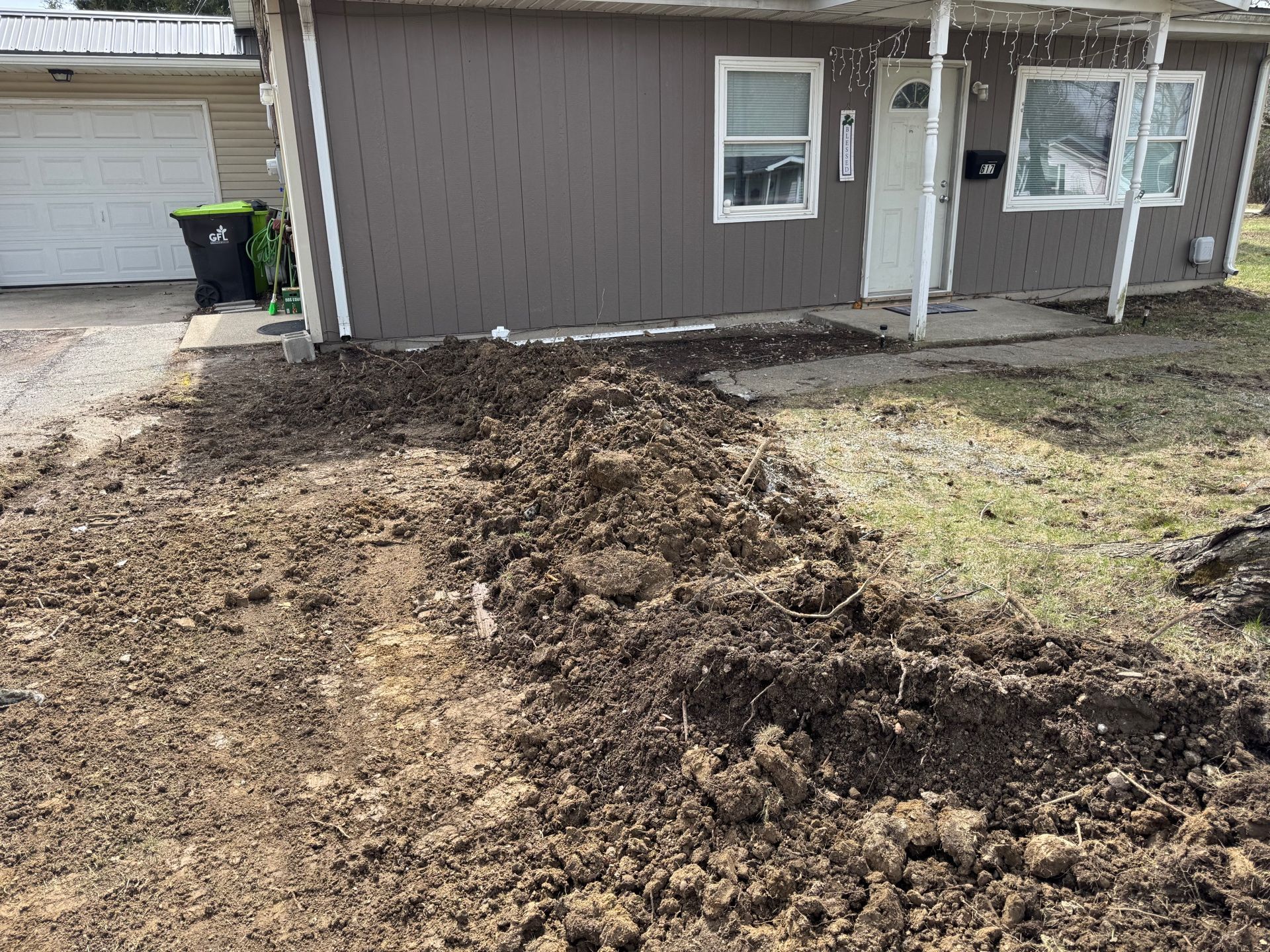 Freshly dug trench of soil beside a gray house with a small yard and windows.