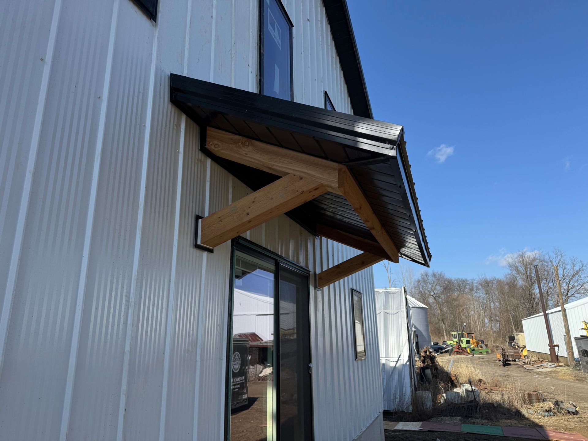 White metal building entrance with glass door and wooden awning under a blue sky