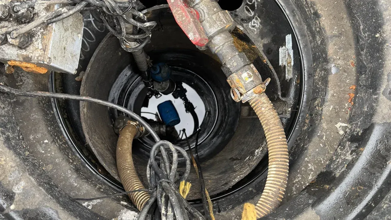 Circular industrial shaft with bundled cables and pipes descending into a dark opening