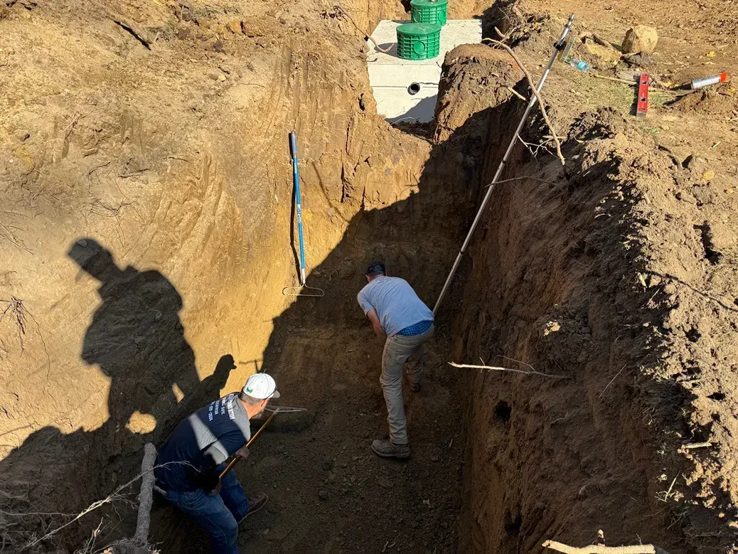 Workers digging a deep trench at a construction site with ropes and equipment
