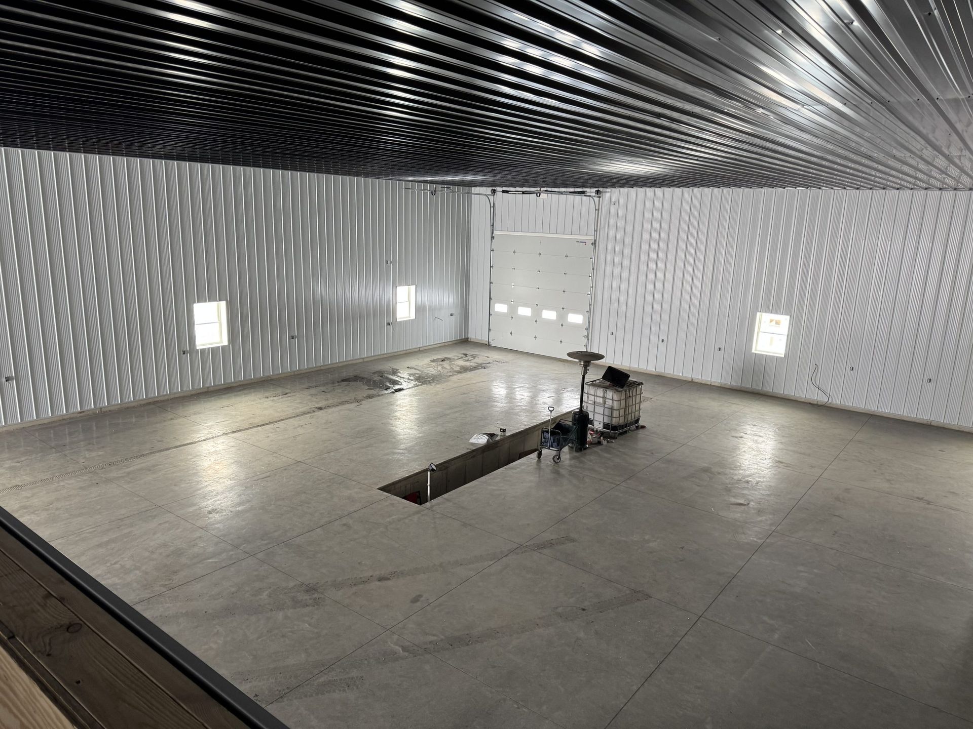Empty industrial room with gray concrete floor, patterned ceiling, wall lights, and a small machine in the center