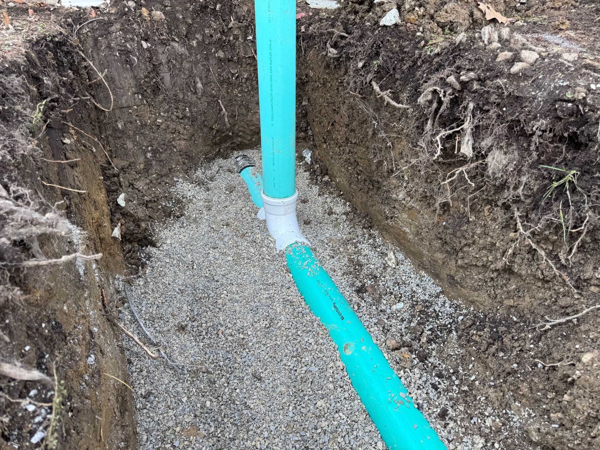 Blue pipe in a gravel trench during excavation, with exposed soil walls.