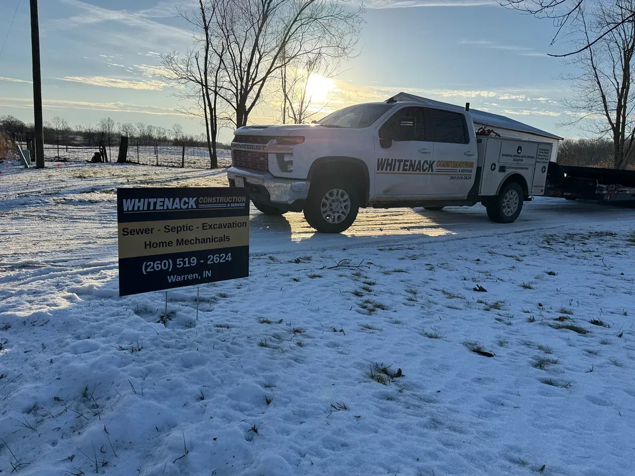 White utility pickup in snowy lot beside a sign at sunset