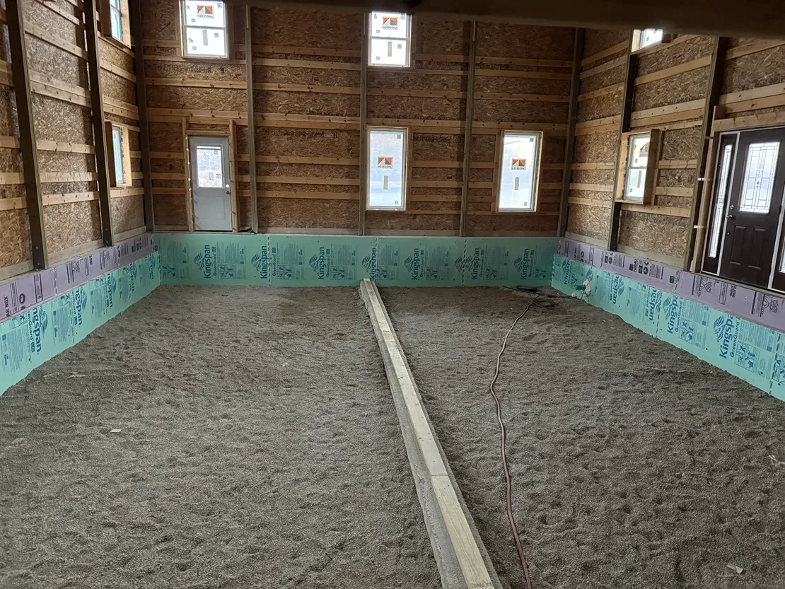 Interior of a rustic barn with two gravel or dirt pens divided by a low center barrier and small windows.