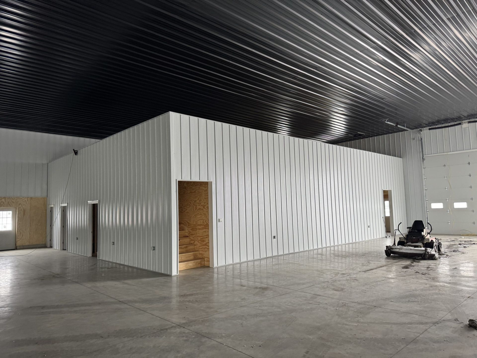 Empty industrial warehouse interior with white walls, black ceiling, and a floor machine near the right wall