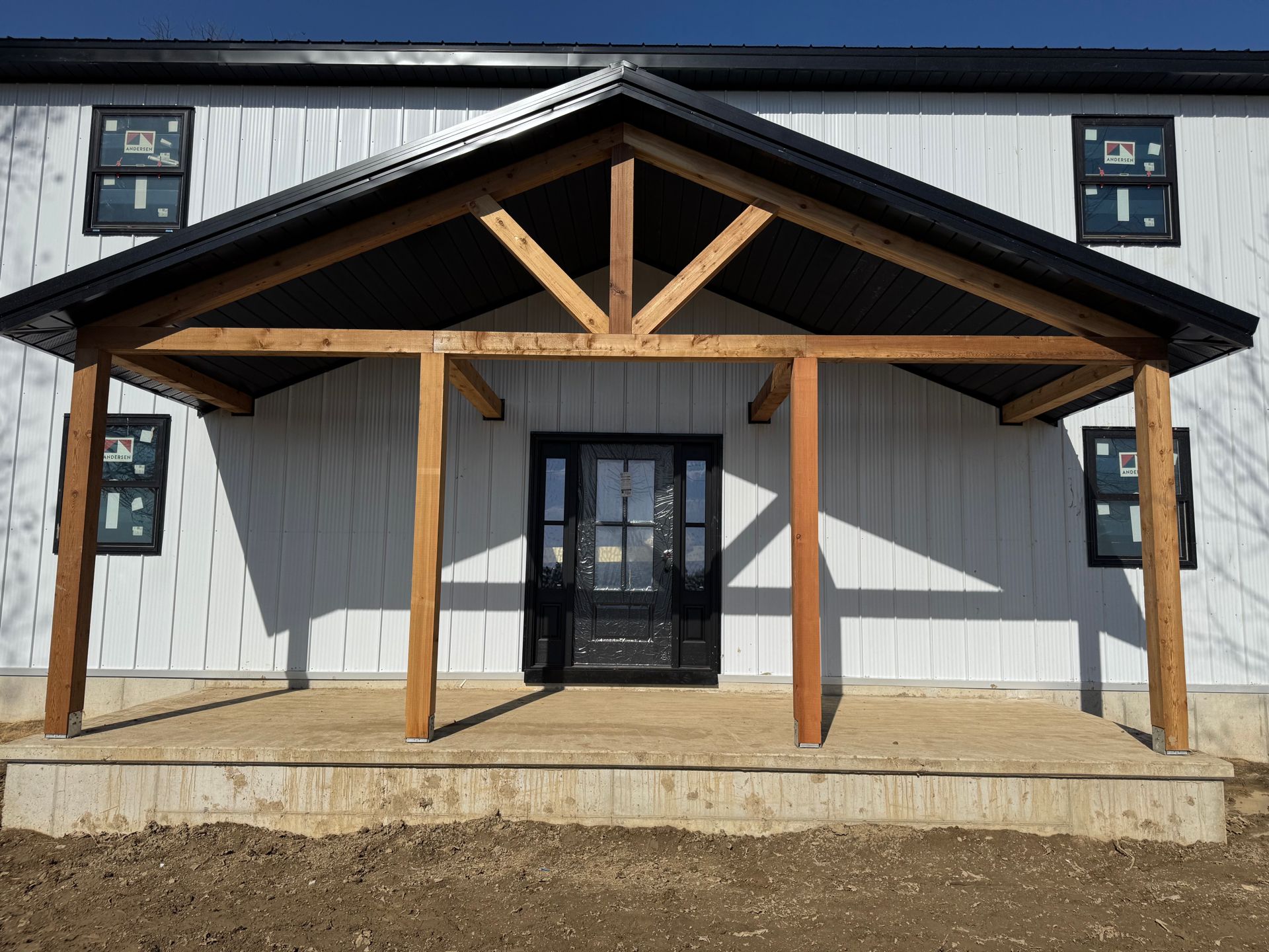Front entrance of a white metal building with a wooden porch and gabled roof.