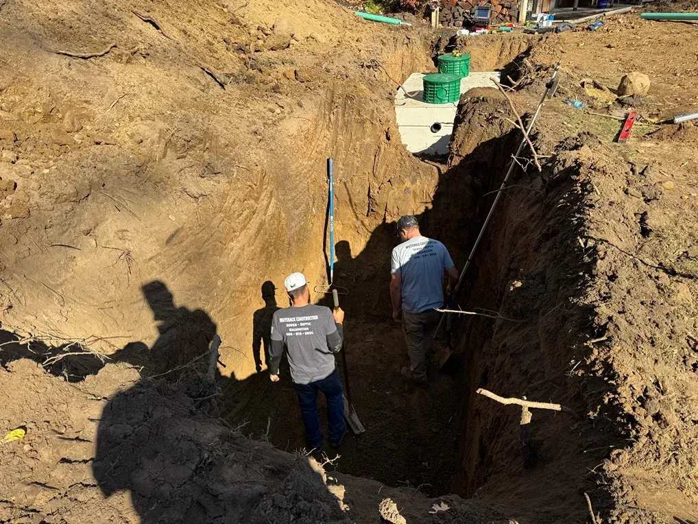 Two workers stand beside a deep dirt trench at a construction site.