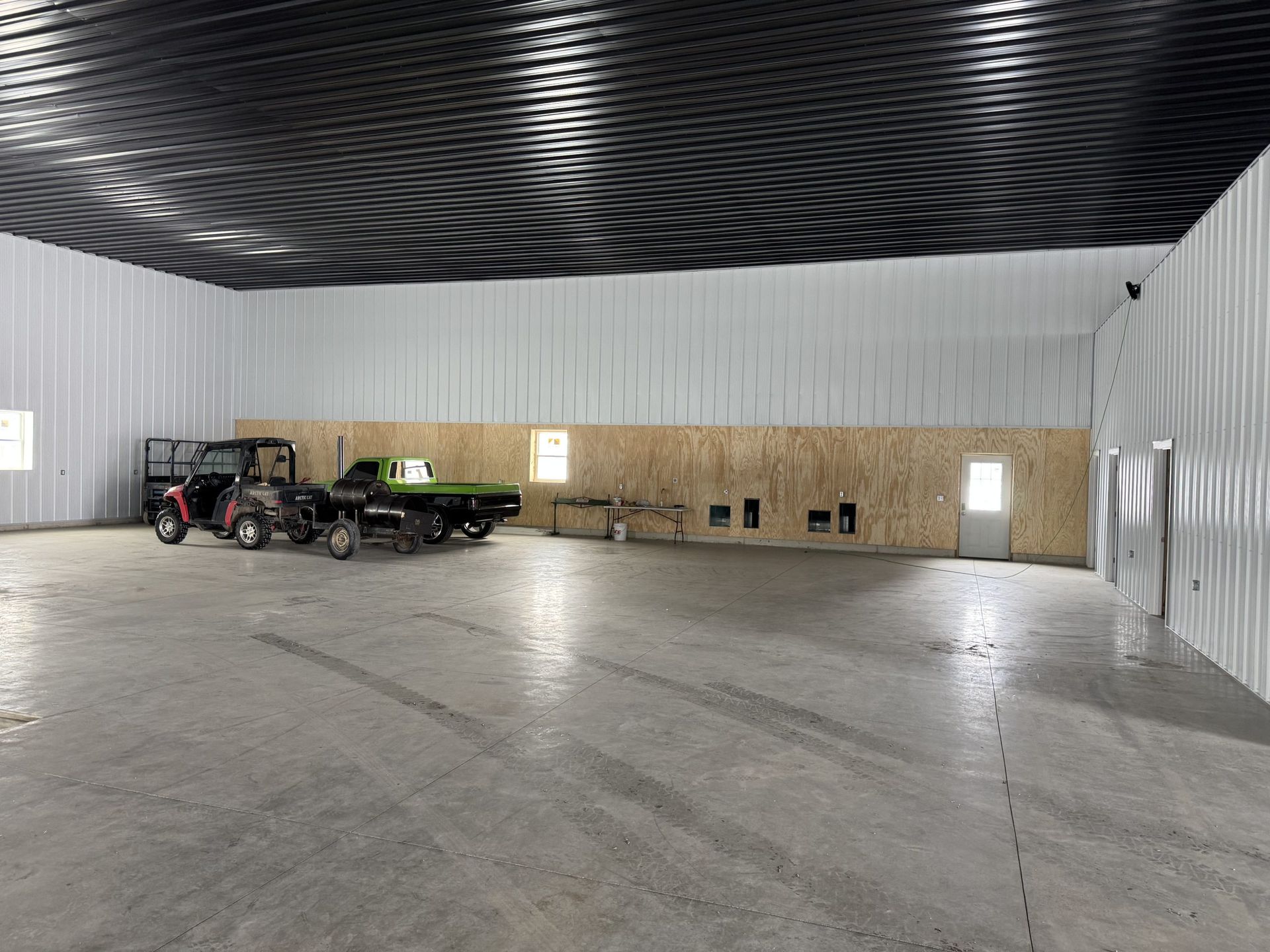 Large empty warehouse interior with a red tractor and green trailer parked along the left wall.