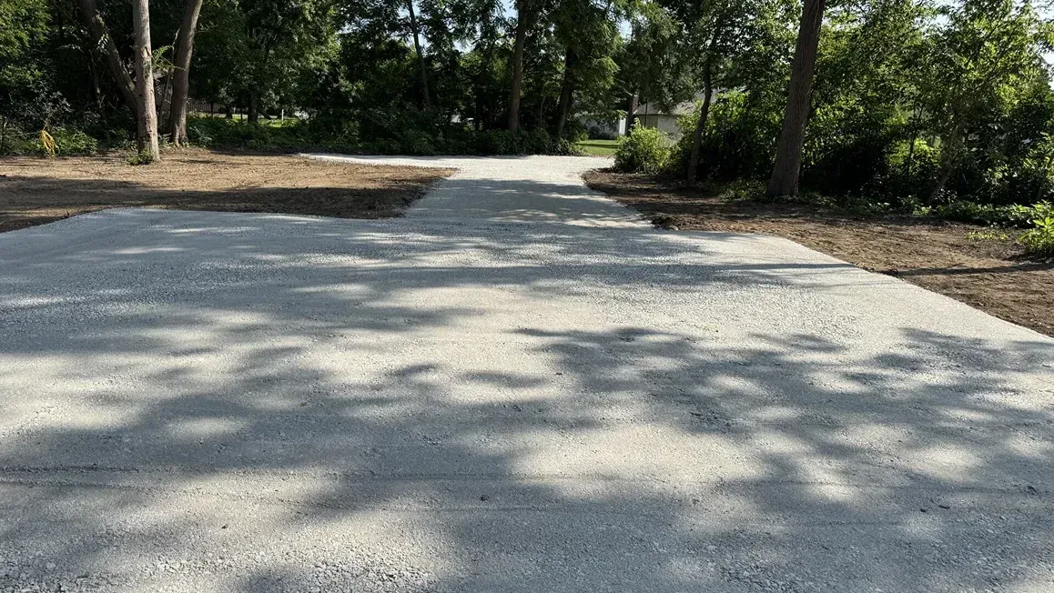 Gravel road curving through a wooded area with sunlight and tree shadows across the path