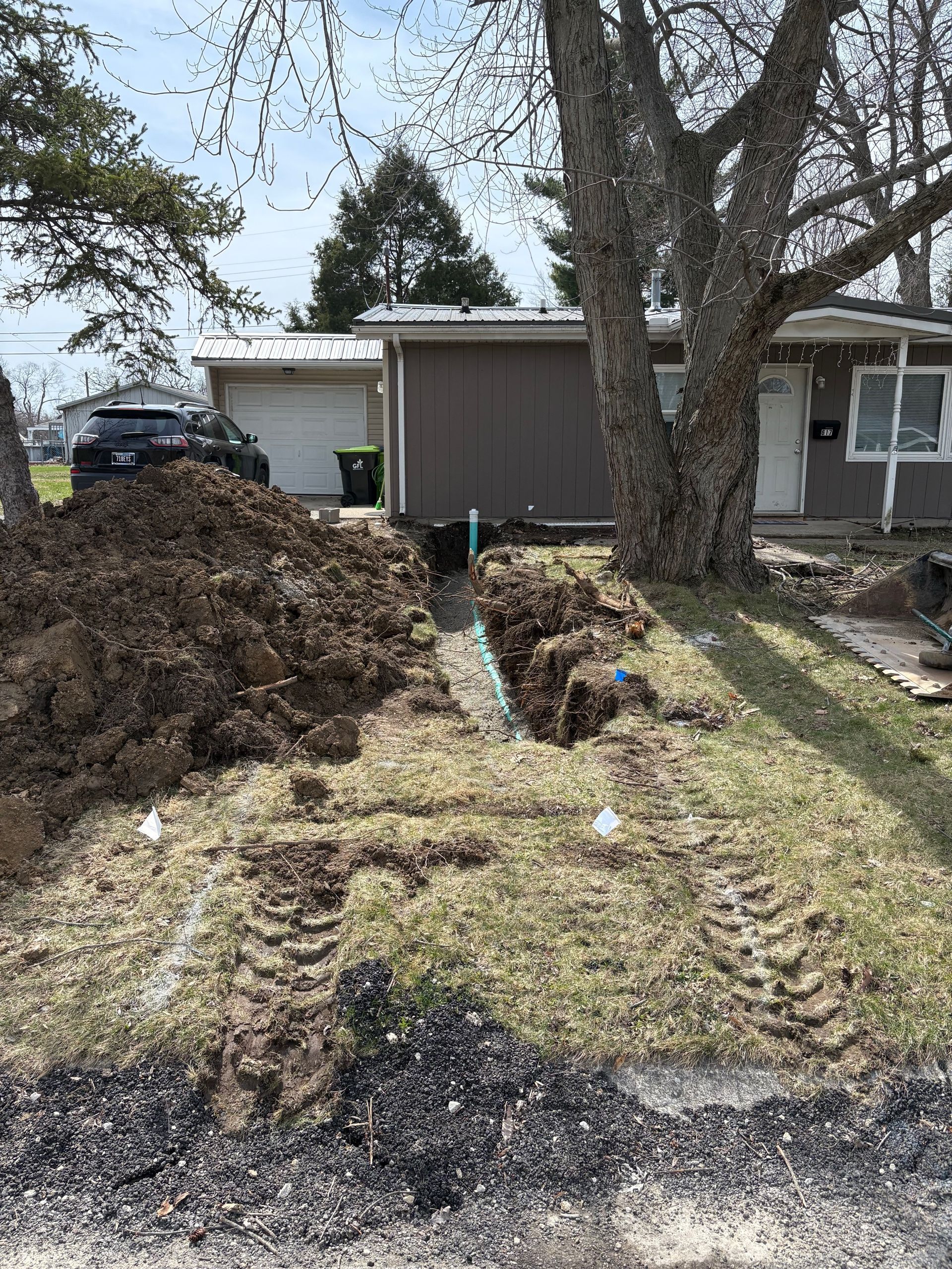 Front yard with a large mulch pile, tree, driveway, and a house in the background after landscaping work.