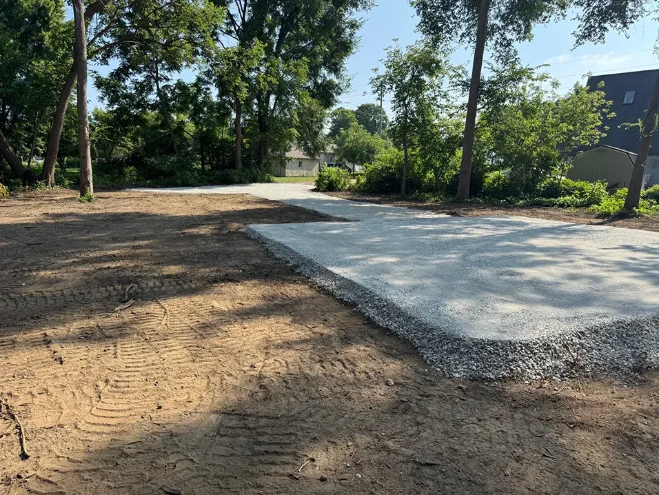 Freshly poured concrete path beside a dirt area and trees in a sunny park-like setting