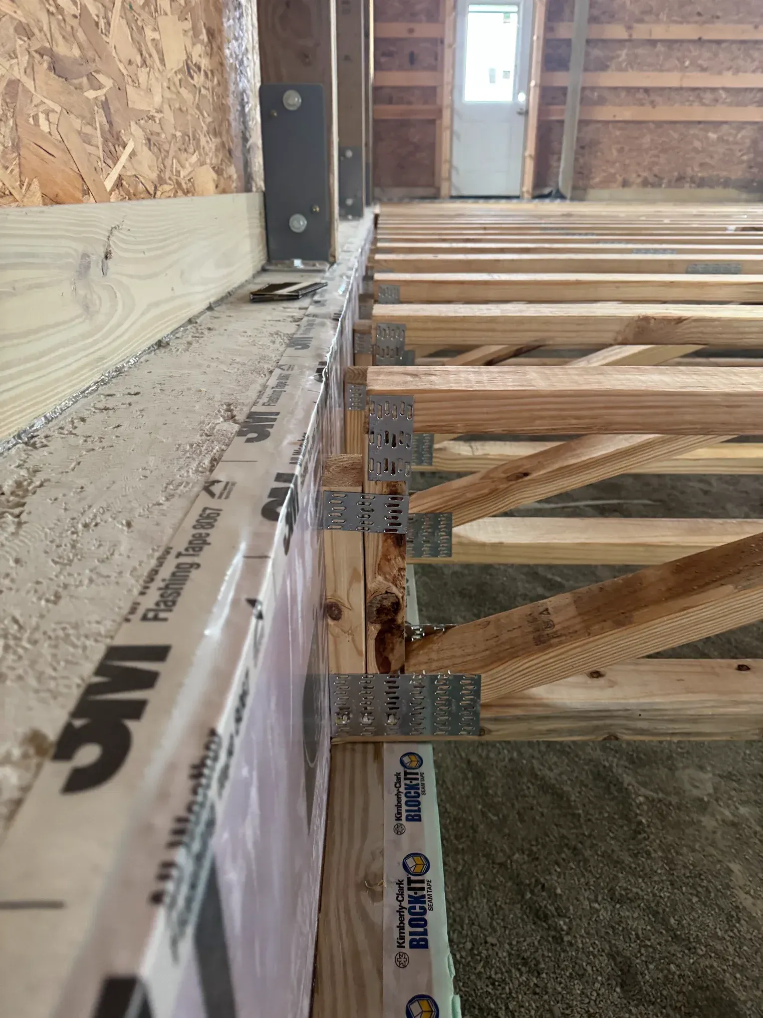 Interior framing of a house under construction, with joists, insulation, and exposed wooden beams.