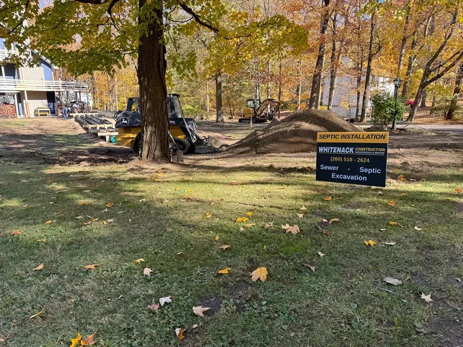 Park lawn with autumn trees and a small sign near a building and parked cars.
