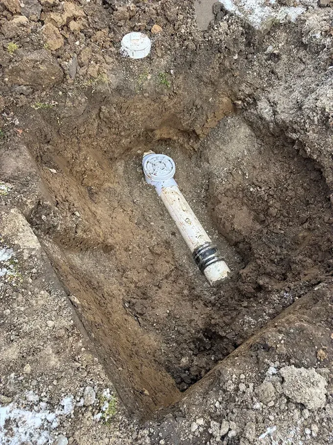 White pipe joint in a dirt excavation trench with a metal connector at one end
