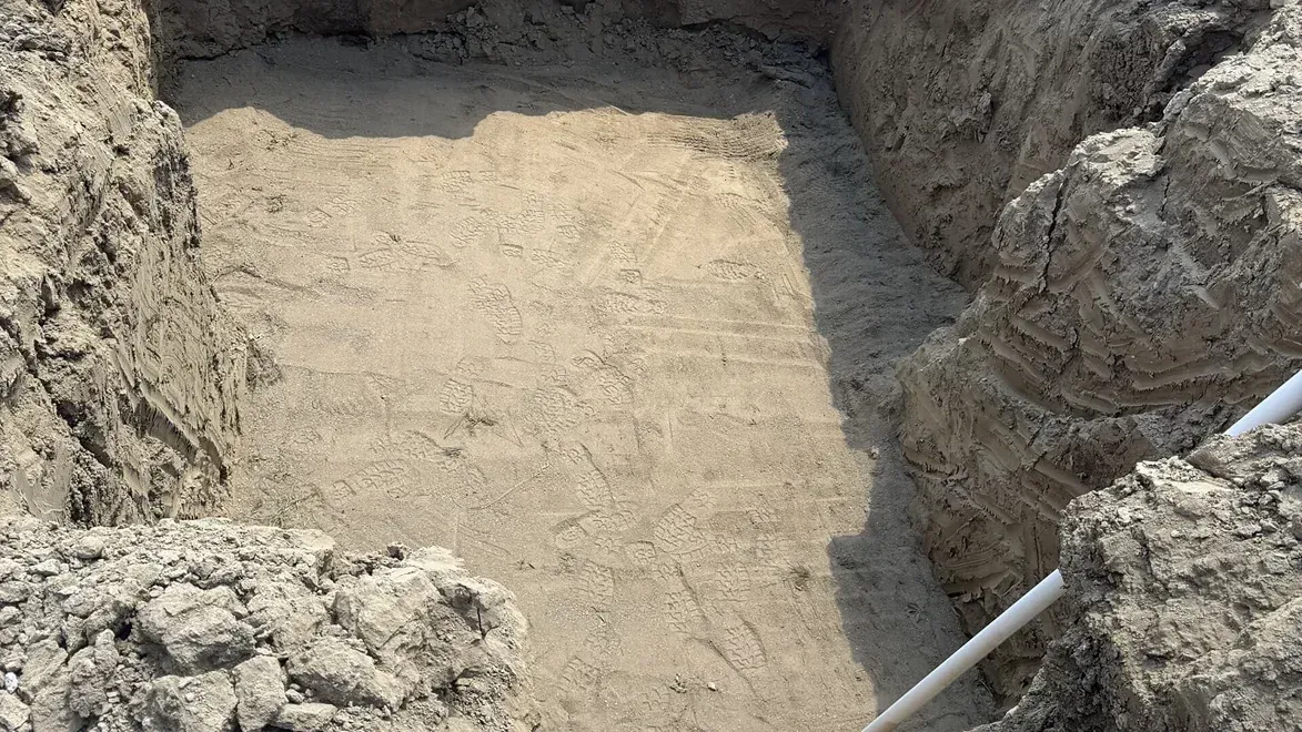 Excavated rectangular dirt pit with rocky walls and a white pipe along the right edge