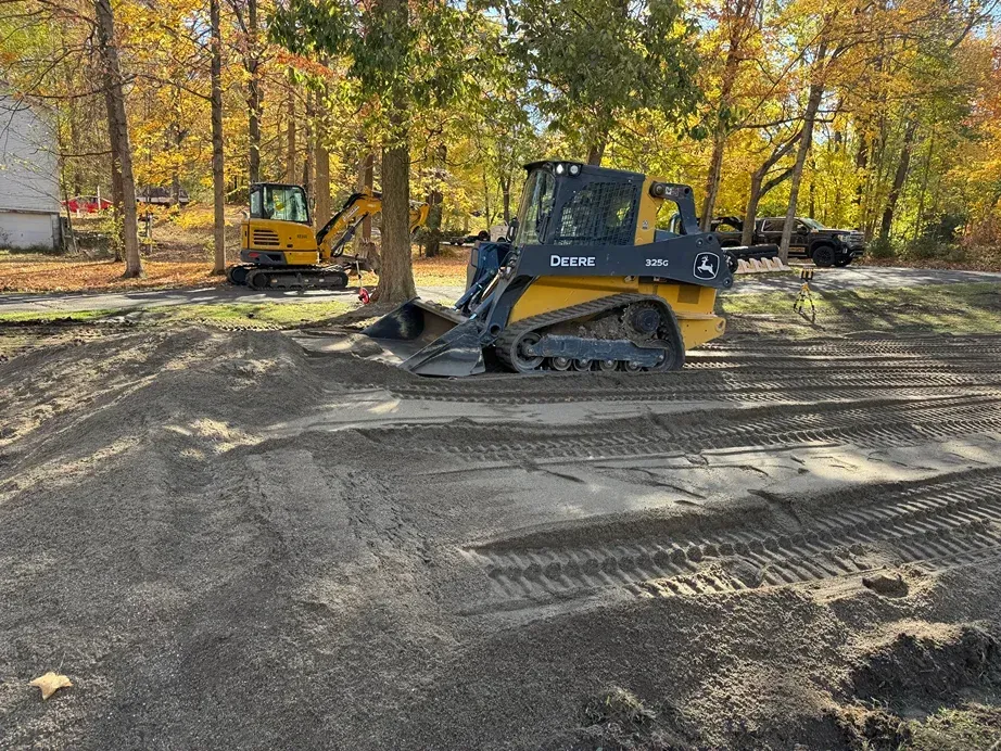 Yellow bulldozer grading a gravel road in a wooded area with autumn trees