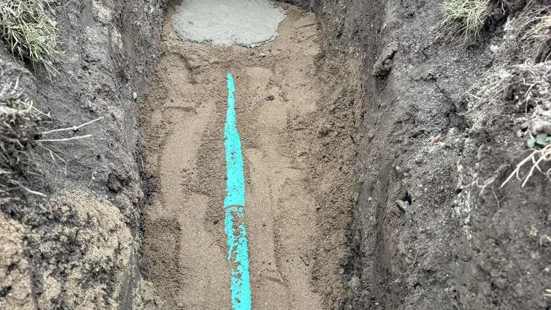 Excavated trench with a blue measuring tape running vertically down the center of the dirt floor.