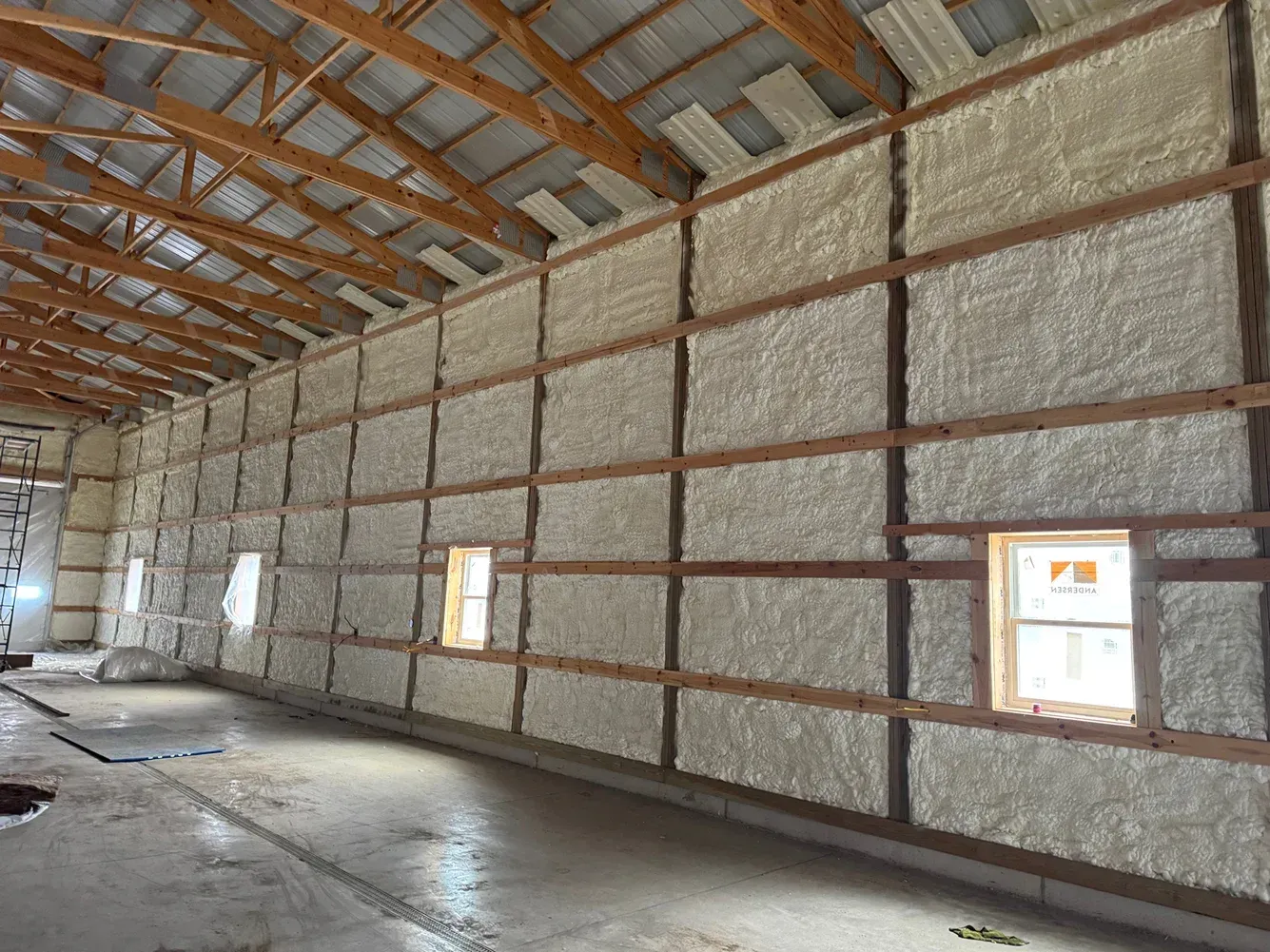 Interior of a large unfinished building with insulated walls, exposed rafters, and small windows.