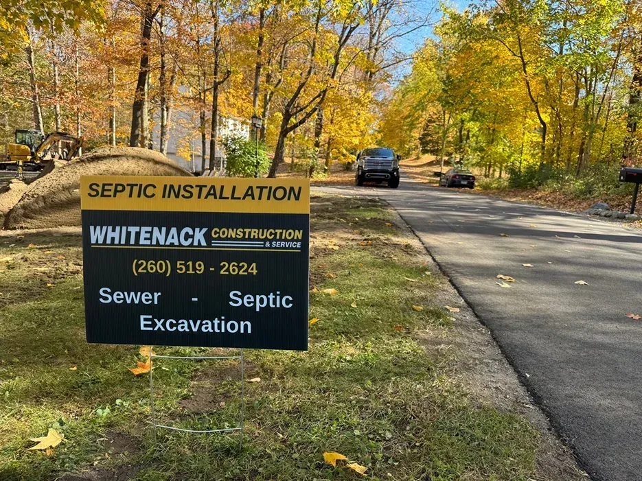 Septic installation sign by a road in autumn, with a truck in the background.