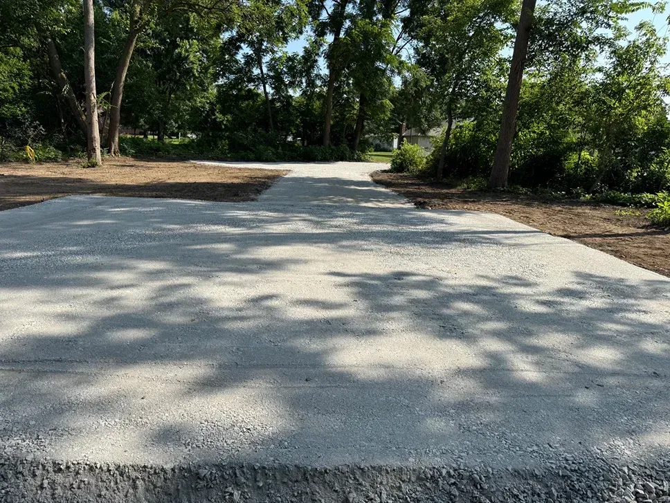 Freshly poured concrete path through a wooded area with trees and dappled sunlight