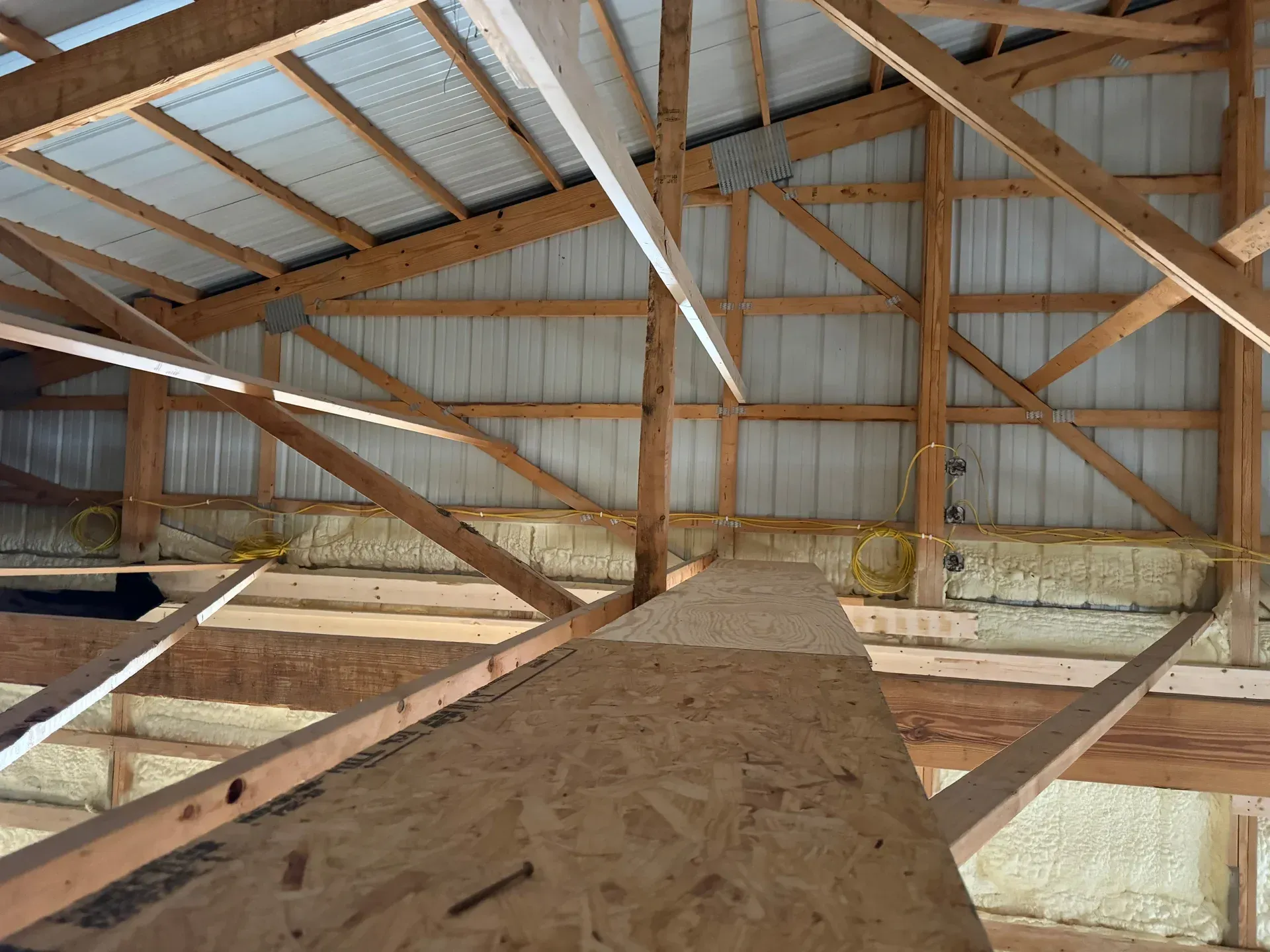 Interior of a barn attic with wooden roof trusses, corrugated metal walls, and an OSB walkway.