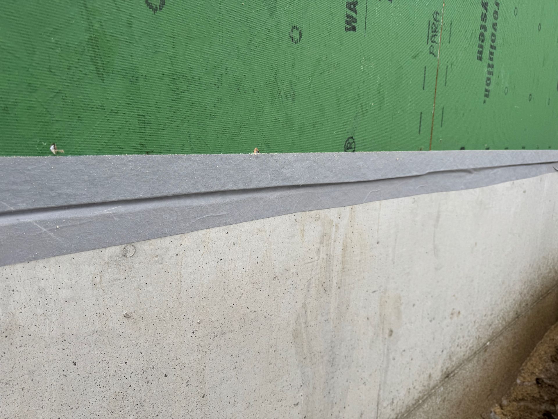 Green insulated wall above a gray slanted ledge with a white concrete base and visible dirt specks