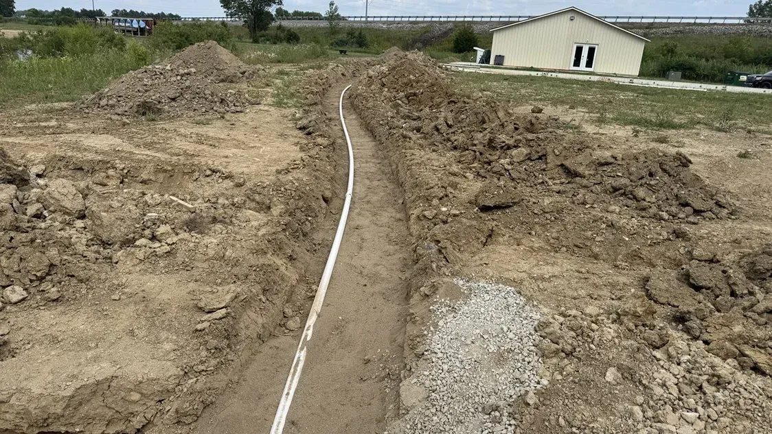 Excavated dirt trench with a white pipe or cable running through a construction site