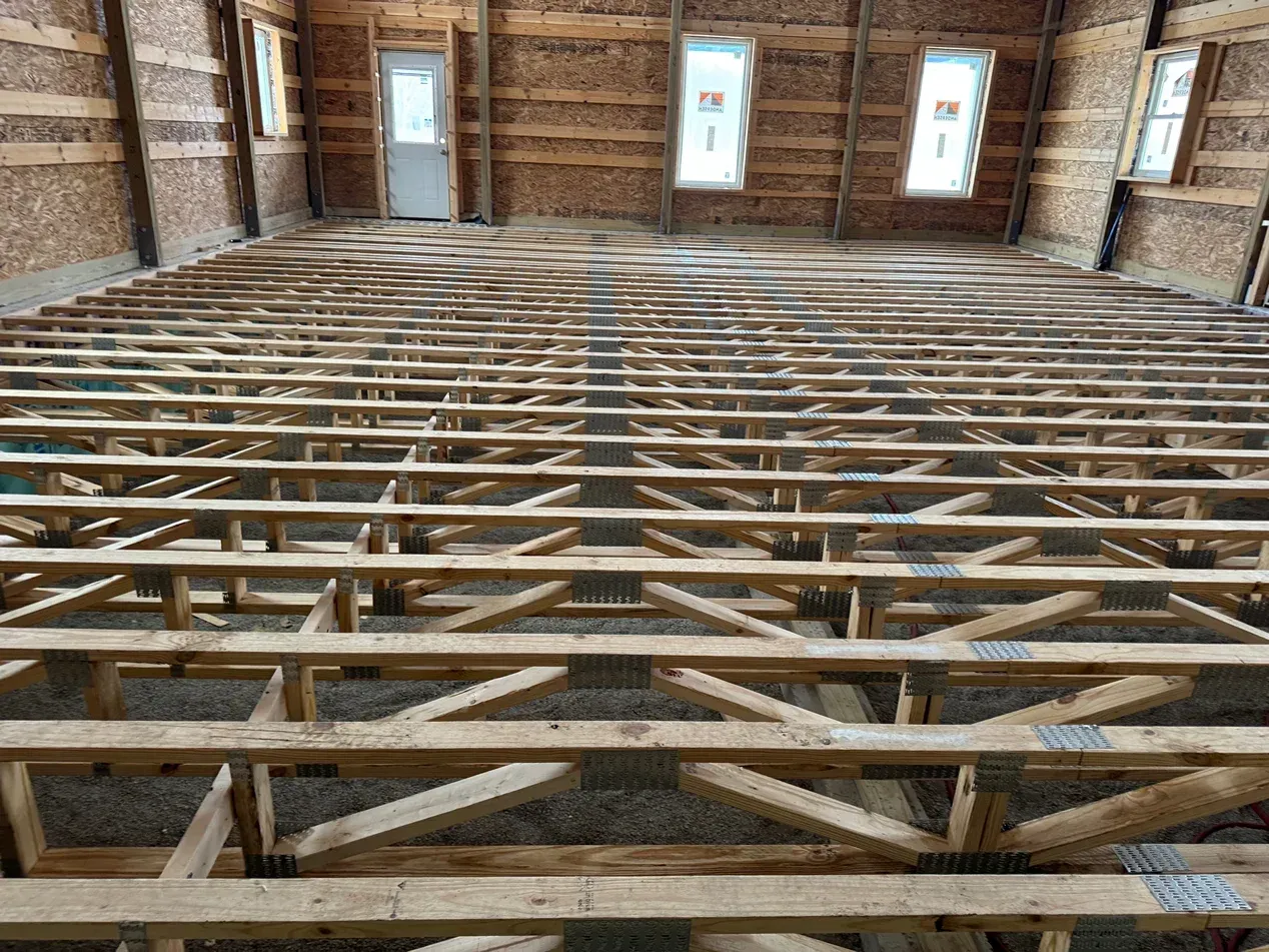 Wooden roof trusses inside an unfinished brick building, viewed from below