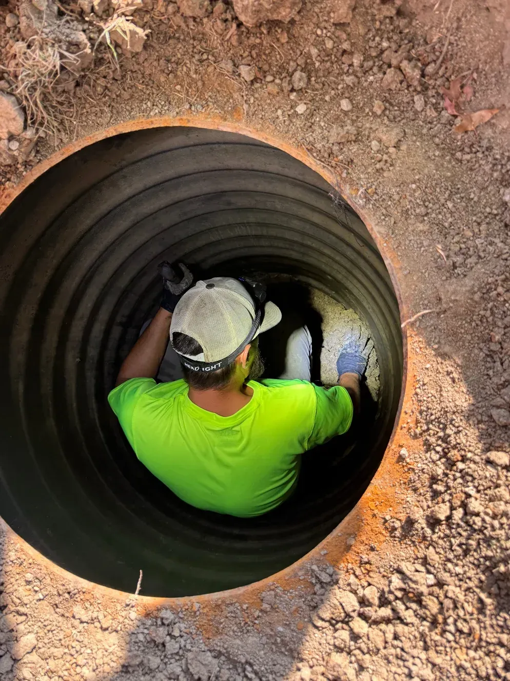 Worker in neon shirt and hard hat inside a large black pipe in a dirt trench