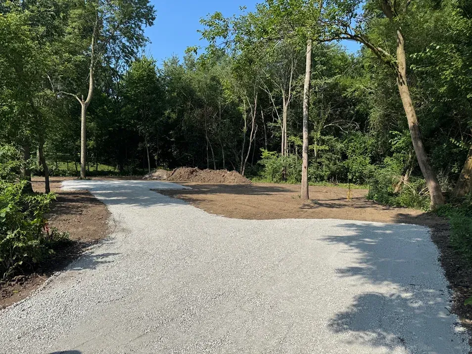Gravel path curving through a wooded area with green trees and bright sunlight