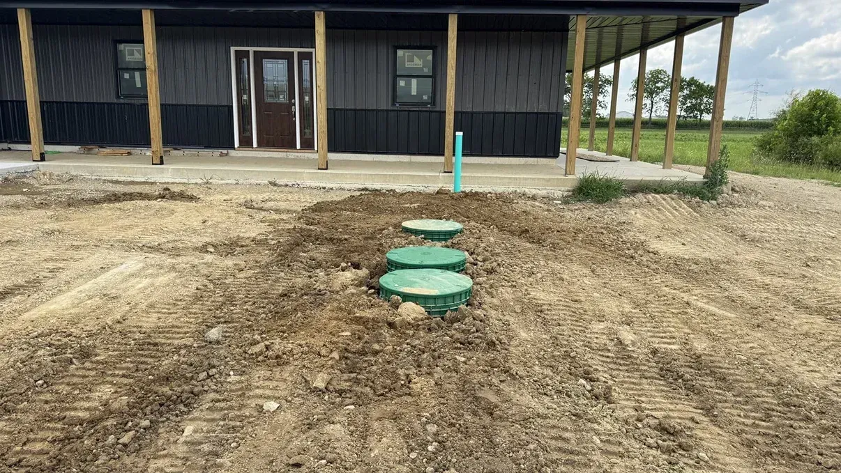 Rural yard with three green septic tank lids and a small building in the background