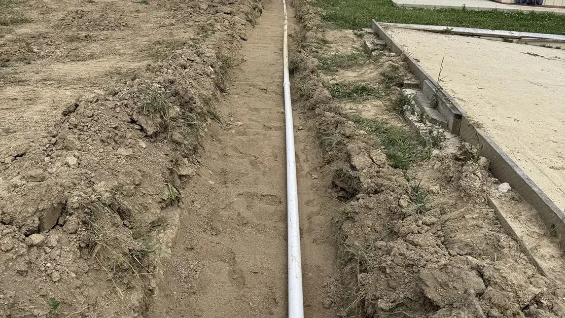 White PVC pipe laid in a dirt trench beside a concrete slab.
