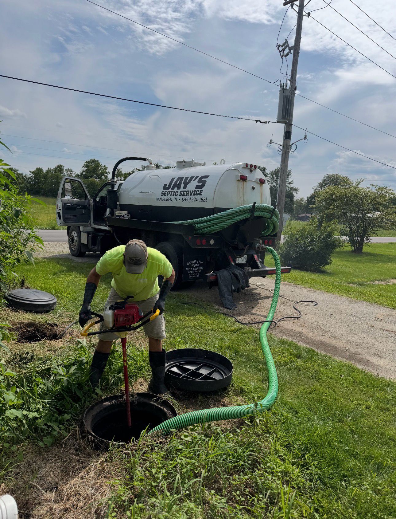 Worker unclogs a sewer line beside a utility truck on a rural road